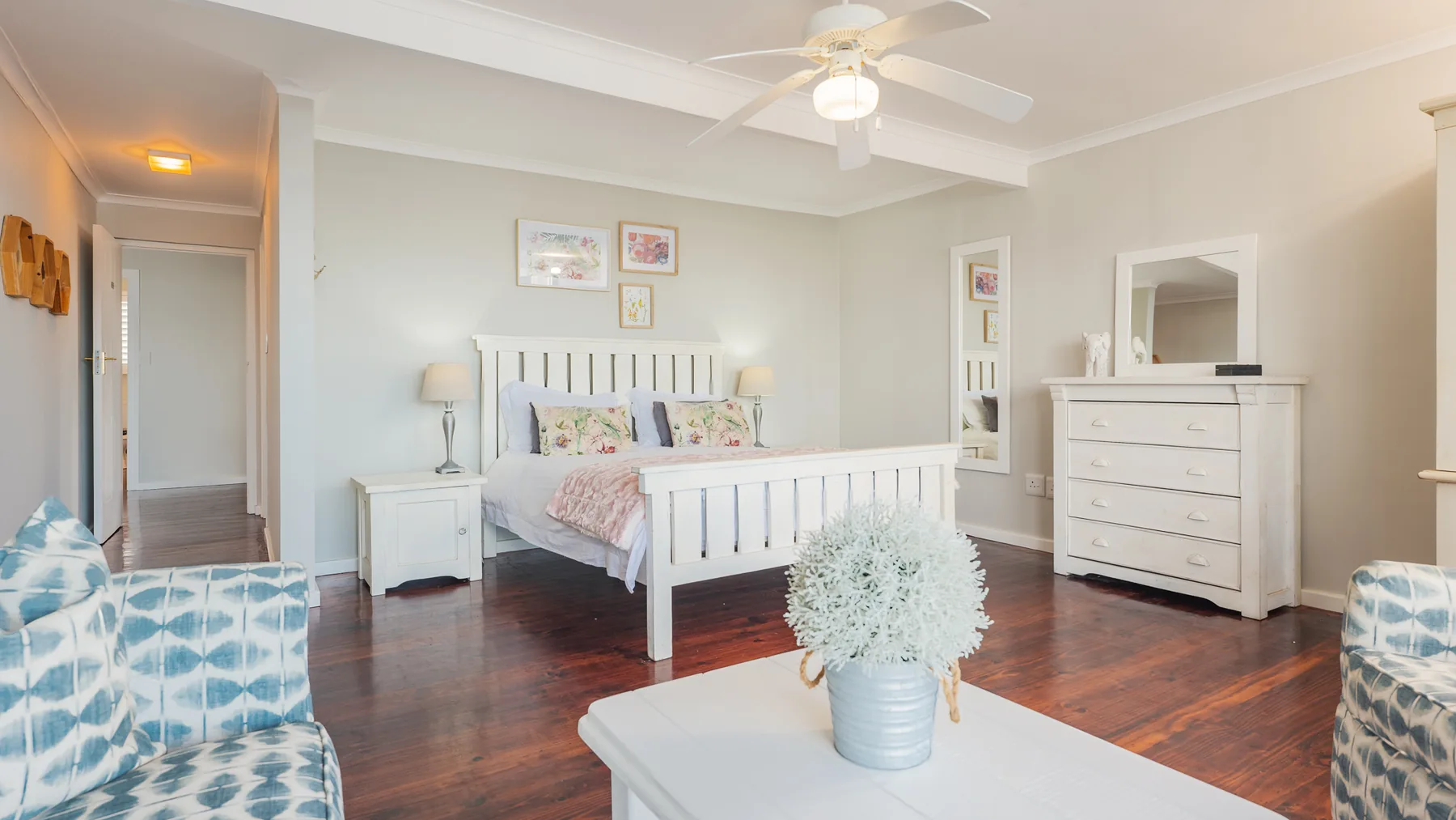 A light and airy bedroom at Driftwood, with white furniture, floral cushions and timber floors