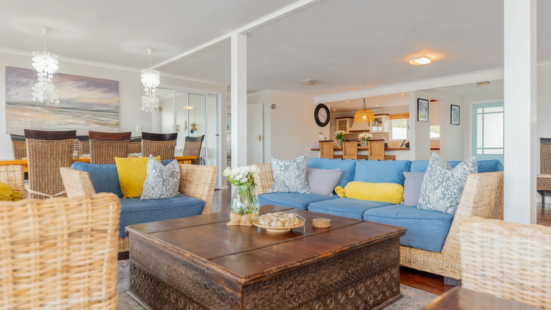 A welcoming shared living and dining area with soft blue sofas, wicker chairs and a warm coastal feel